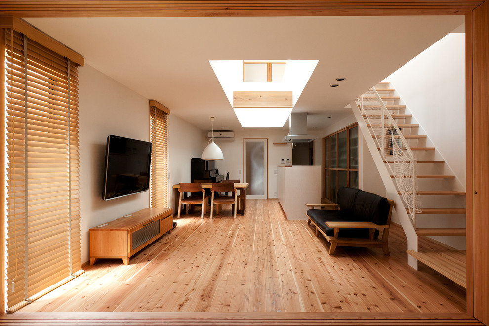 Пример оригинального дизайна: открытая гостиная комната в восточном стиле с белыми стенами, светлым паркетным полом и телевизором на стене