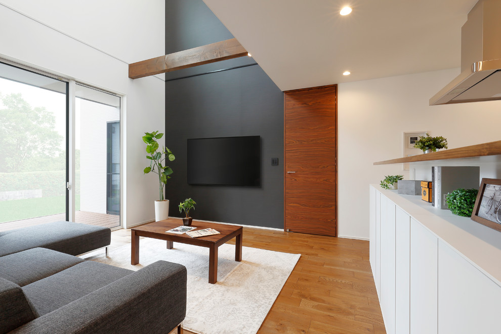 Cette photo montre un salon asiatique ouvert avec un mur blanc, un sol en bois brun, un téléviseur fixé au mur et un sol marron.