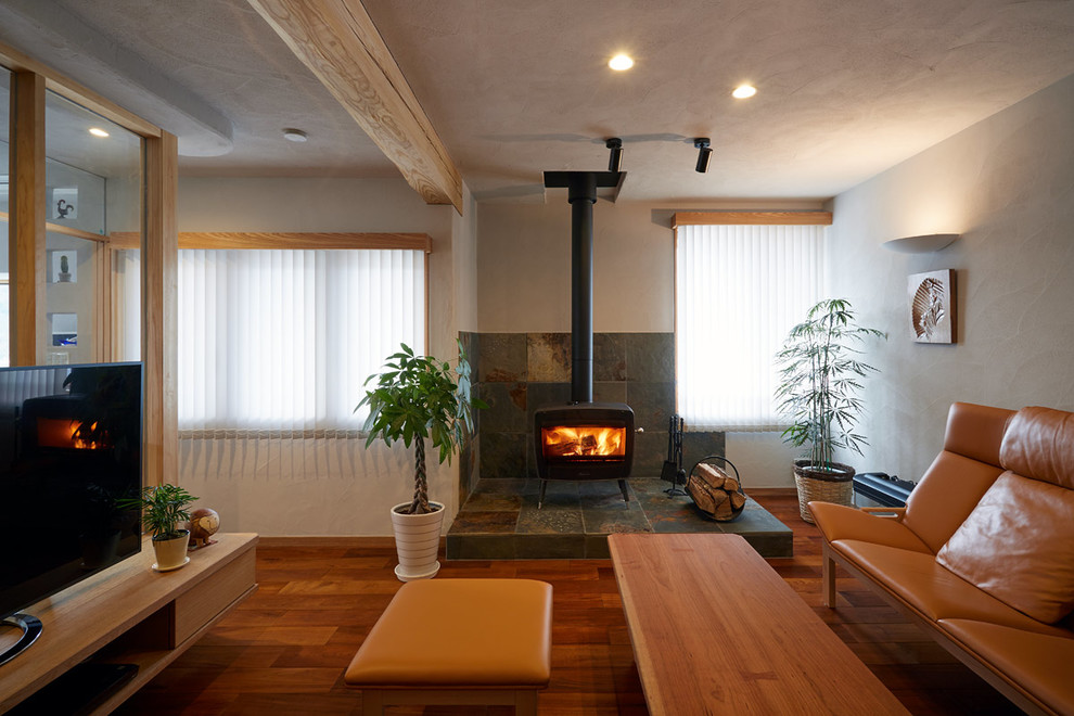 Immagine di un soggiorno etnico con pavimento in legno massello medio, stufa a legna, cornice del camino in pietra, pareti bianche, TV autoportante e pavimento marrone