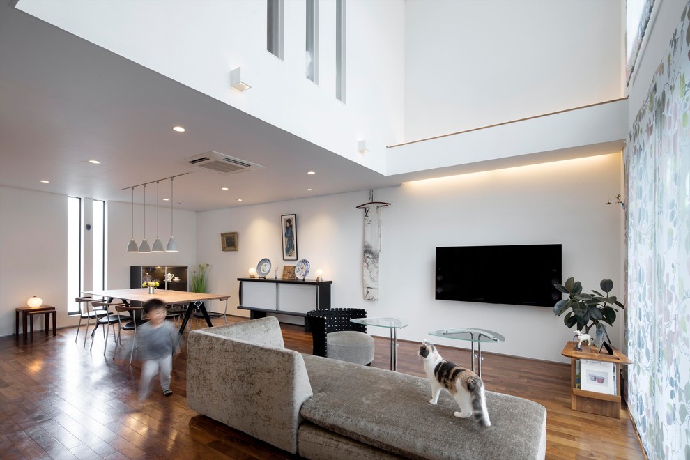 Идея дизайна: гостиная комната в современном стиле с белыми стенами, паркетным полом среднего тона, телевизором на стене и коричневым полом