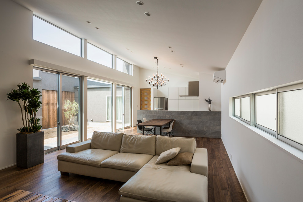Aménagement d'un salon moderne ouvert avec un mur blanc, parquet foncé et un sol marron.