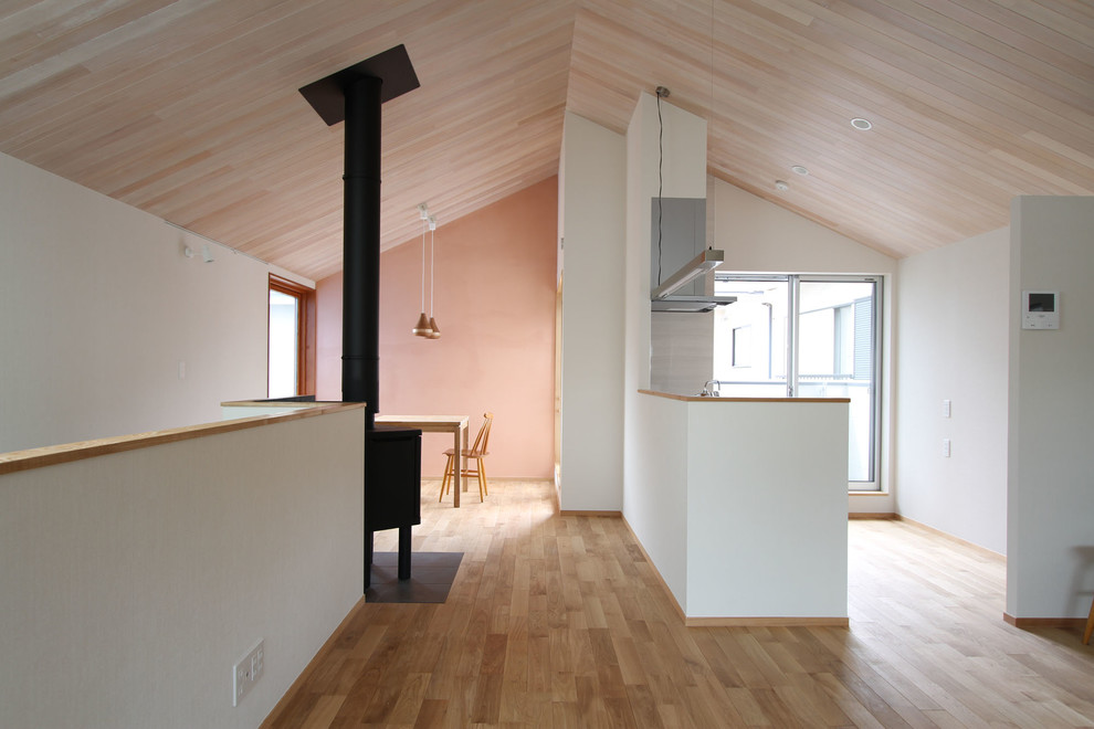 Offenes Modernes Wohnzimmer mit rosa Wandfarbe, braunem Holzboden, Kaminofen, Kaminumrandung aus Metall, freistehendem TV und braunem Boden in Tokio