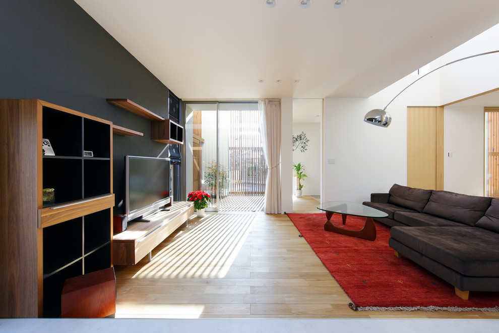 Modelo de salón abierto asiático de tamaño medio con paredes negras, suelo de madera en tonos medios, televisor independiente y suelo marrón
