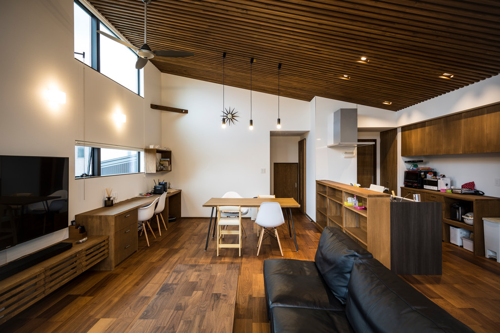 Offenes Asiatisches Wohnzimmer mit weißer Wandfarbe, braunem Holzboden, freistehendem TV und braunem Boden in Sonstige