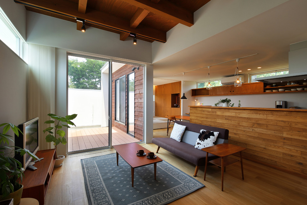 Offenes Asiatisches Wohnzimmer mit weißer Wandfarbe, hellem Holzboden, freistehendem TV und braunem Boden in Sonstige