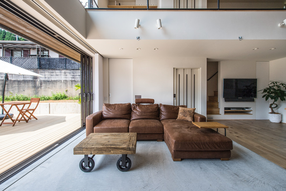 Foto di un soggiorno industriale aperto con pareti bianche, pavimento in cemento, TV a parete e pavimento grigio
