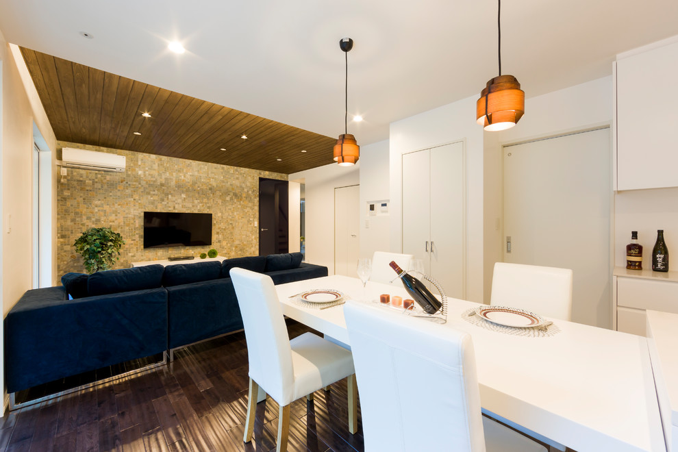 Пример оригинального дизайна: открытая гостиная комната в современном стиле с белыми стенами, темным паркетным полом, телевизором на стене и коричневым полом