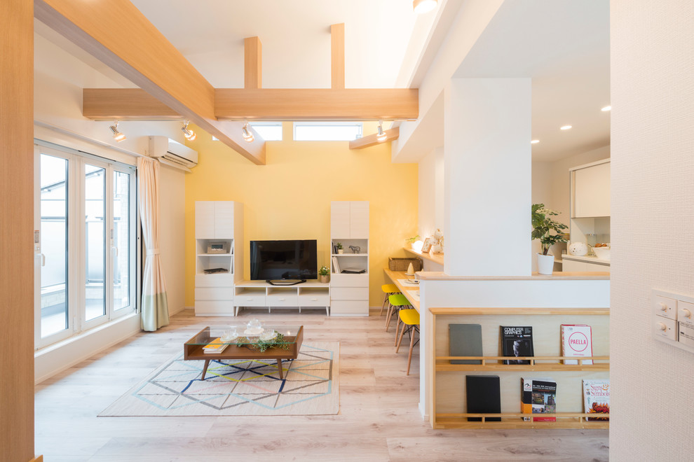Foto på ett nordiskt vardagsrum, med gula väggar, en fristående TV, grått golv och ljust trägolv