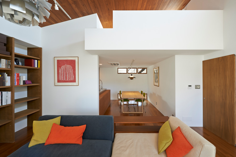 Modelo de salón abierto retro sin chimenea con paredes blancas y suelo de madera en tonos medios