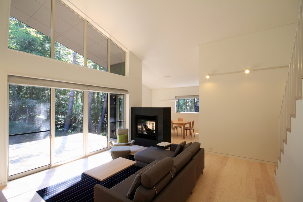 Источник вдохновения для домашнего уюта: открытая гостиная комната среднего размера в стиле модернизм с белыми стенами, полом из фанеры, двусторонним камином, фасадом камина из камня и коричневым полом