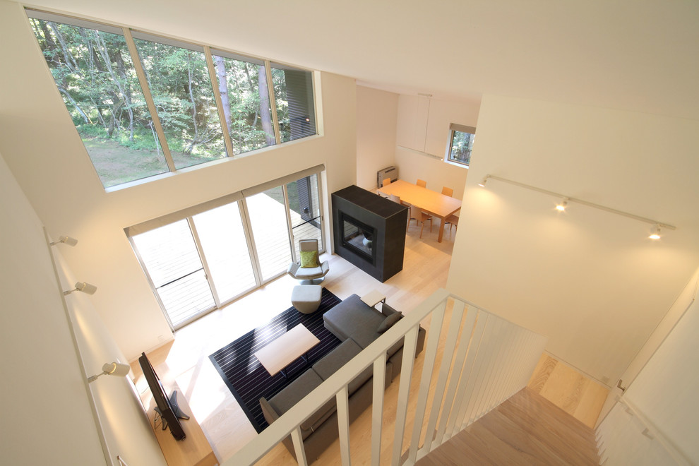 Пример оригинального дизайна: открытая гостиная комната среднего размера в стиле модернизм с белыми стенами, полом из фанеры, двусторонним камином, фасадом камина из камня и коричневым полом