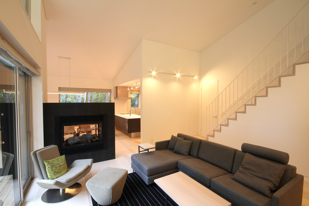 Стильный дизайн: открытая гостиная комната среднего размера в стиле модернизм с белыми стенами, полом из фанеры, двусторонним камином, фасадом камина из камня и коричневым полом - последний тренд