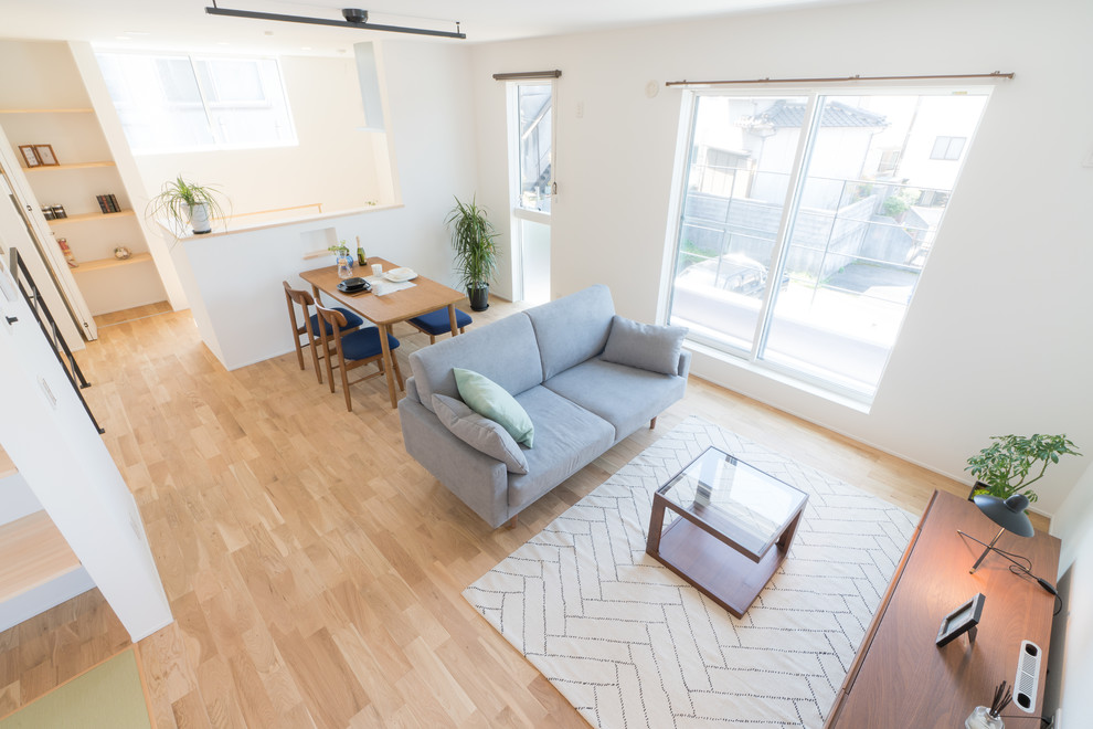 Modelo de salón abierto minimalista pequeño sin chimenea con paredes blancas, suelo de madera clara y televisor independiente