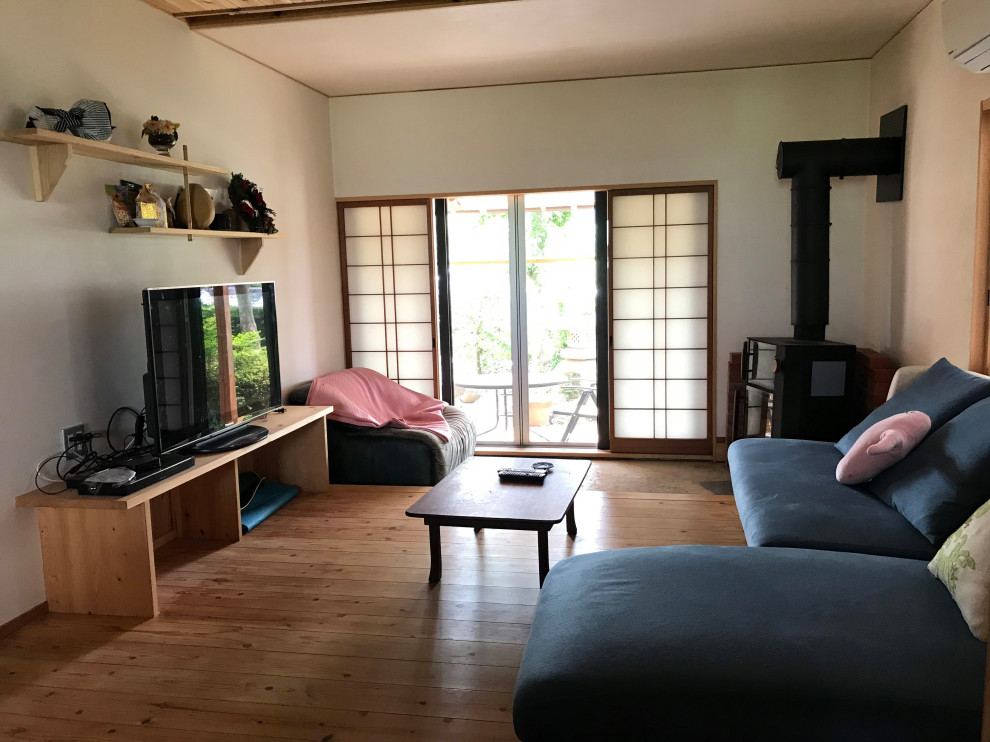 Réalisation d'un petit salon asiatique ouvert avec une salle de réception, un mur blanc, parquet clair, un poêle à bois, un manteau de cheminée en plâtre et un téléviseur indépendant.
