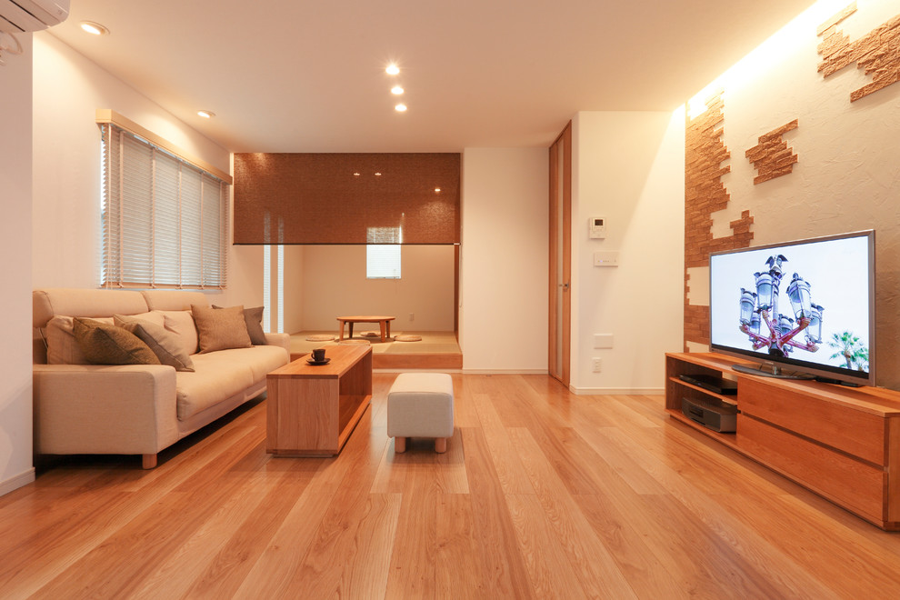 Modernes Wohnzimmer mit weißer Wandfarbe, hellem Holzboden, freistehendem TV und beigem Boden in Sonstige