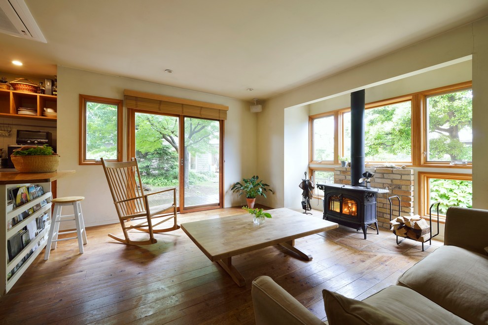 Cette photo montre un grand salon nature ouvert avec un mur blanc, un sol en bois brun, un poêle à bois, un manteau de cheminée en brique, aucun téléviseur et un sol beige.