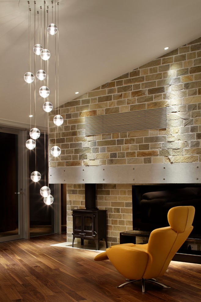 Diseño de salón actual sin televisor con paredes marrones, suelo de madera en tonos medios, estufa de leña y marco de chimenea de ladrillo