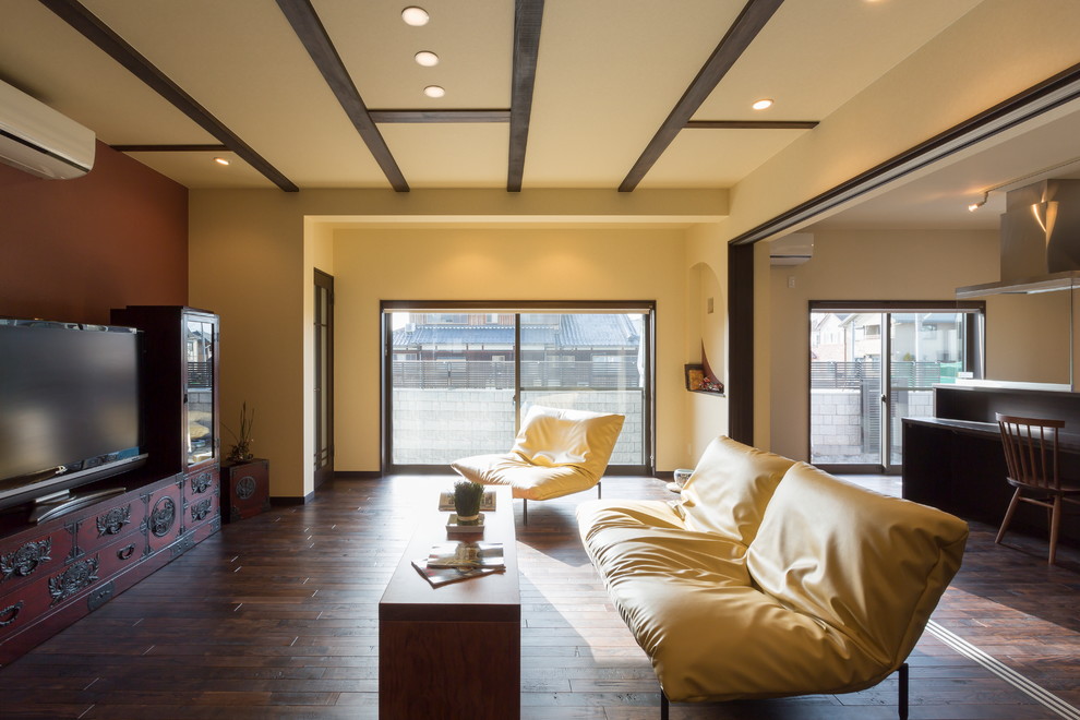 Offenes Asiatisches Wohnzimmer mit bunten Wänden, dunklem Holzboden, freistehendem TV und braunem Boden in Sonstige