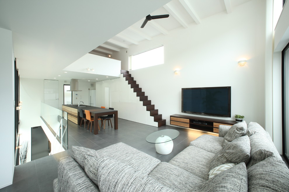 Modelo de salón para visitas abierto minimalista grande sin chimenea con paredes blancas, suelo de pizarra y televisor colgado en la pared