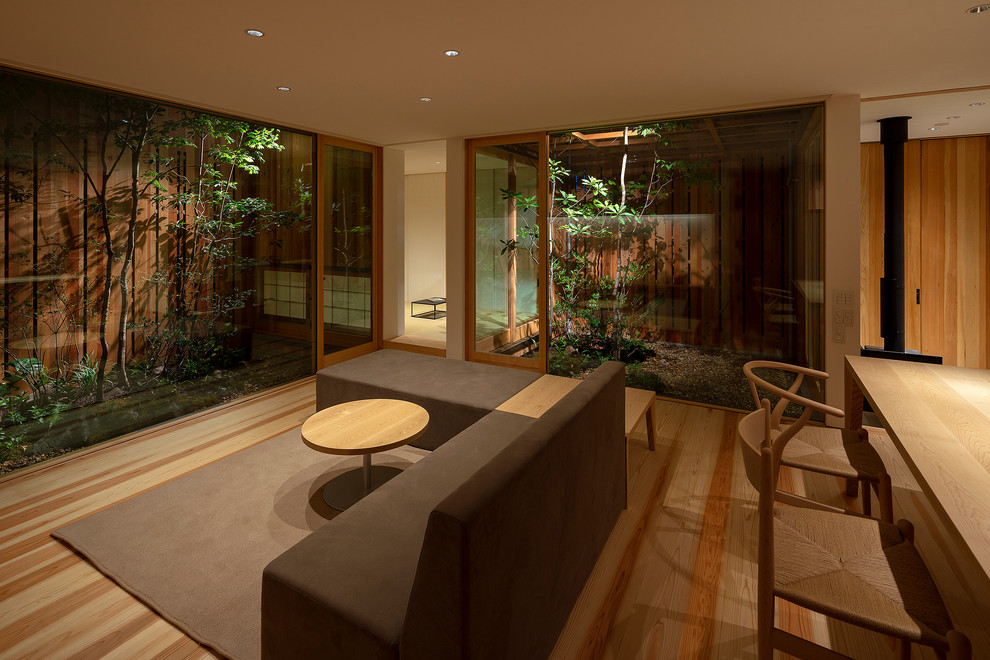 Modelo de salón asiático sin televisor con paredes blancas, suelo de madera en tonos medios, estufa de leña y marco de chimenea de hormigón