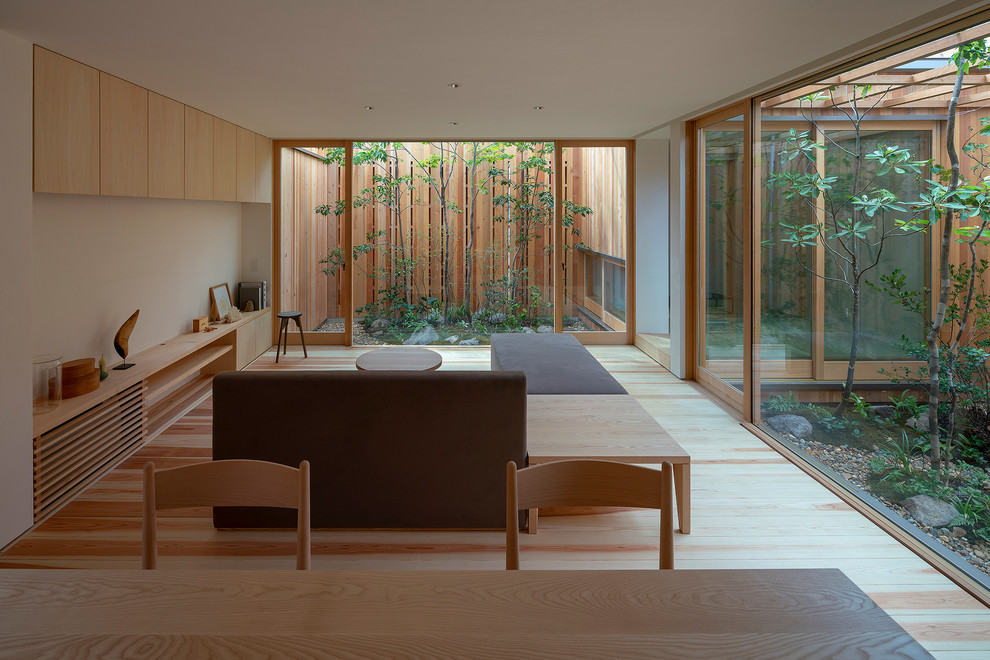 Diseño de salón abierto asiático de tamaño medio con paredes blancas, suelo de madera clara, suelo marrón y televisor colgado en la pared