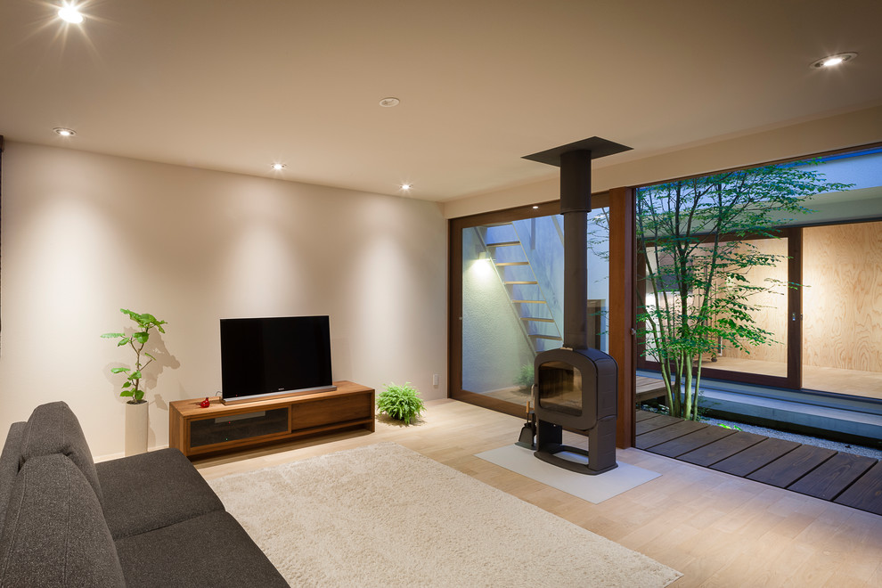 Modelo de salón de estilo zen con paredes blancas, suelo de madera clara, televisor independiente y suelo beige