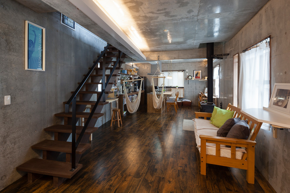 Cette photo montre un grand salon industriel ouvert avec un mur gris, un sol en vinyl, un poêle à bois, un manteau de cheminée en carrelage et un sol noir.