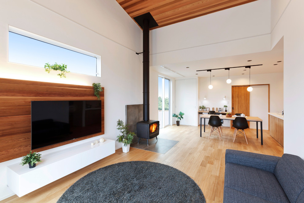 Modern inredning av ett vardagsrum, med vita väggar, mellanmörkt trägolv, en öppen vedspis, en spiselkrans i trä, en väggmonterad TV och brunt golv