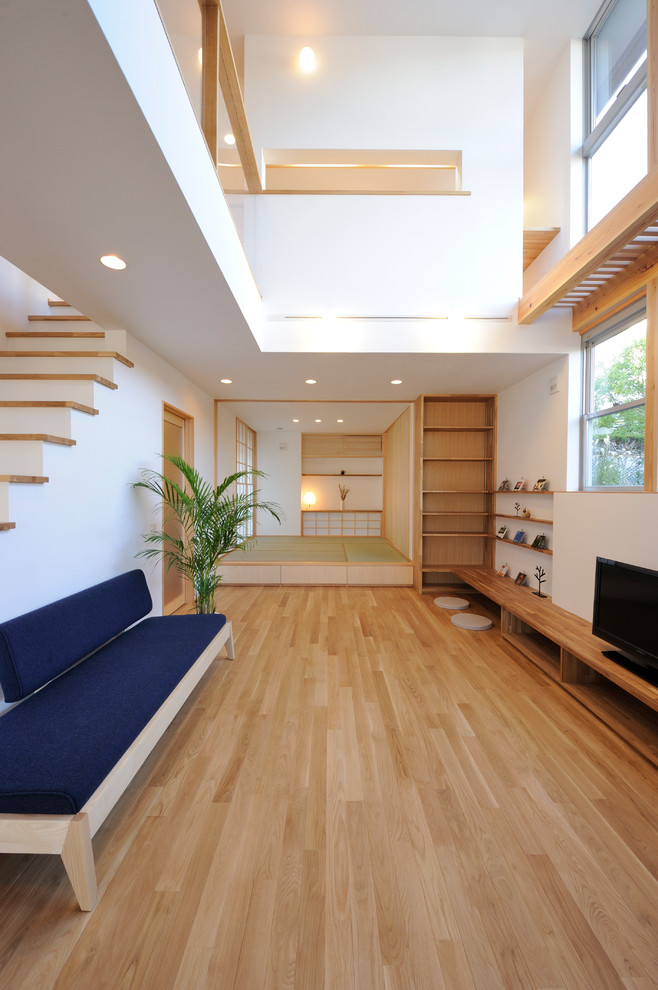 Modelo de salón abierto nórdico con paredes blancas, suelo de madera en tonos medios, televisor independiente y suelo marrón