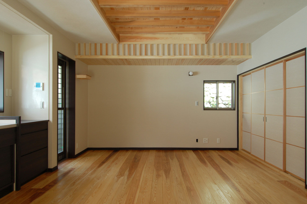 Diseño de salón abierto asiático con paredes blancas, suelo de madera clara, televisor colgado en la pared y suelo marrón