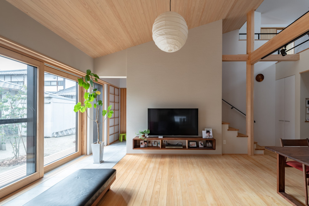 Ejemplo de salón abierto asiático de tamaño medio sin chimenea con paredes blancas, suelo de madera clara, televisor colgado en la pared y madera