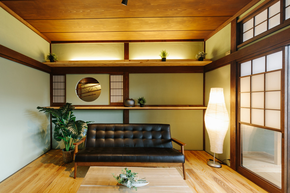 Réalisation d'un salon avec un mur vert, un sol en bois brun, aucun téléviseur, un sol beige et canapé noir.