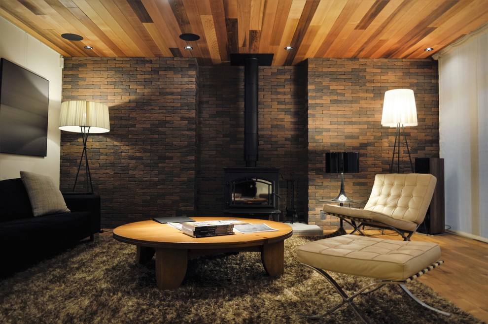 Idées déco pour un salon rétro avec un mur blanc, un sol en bois brun, un poêle à bois, un manteau de cheminée en brique et un sol marron.