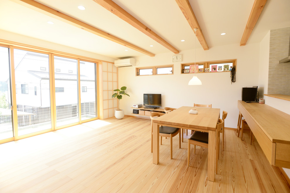 Asiatisches Wohnzimmer mit weißer Wandfarbe, braunem Holzboden, freistehendem TV und braunem Boden in Sonstige
