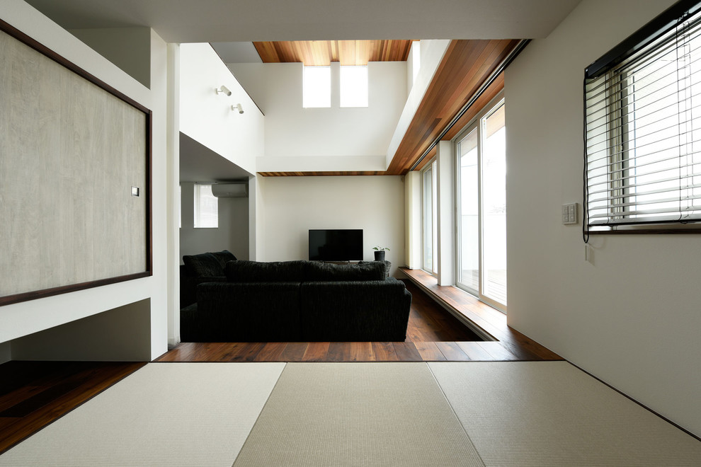 Offenes Modernes Wohnzimmer ohne Kamin mit weißer Wandfarbe, dunklem Holzboden und freistehendem TV in Osaka