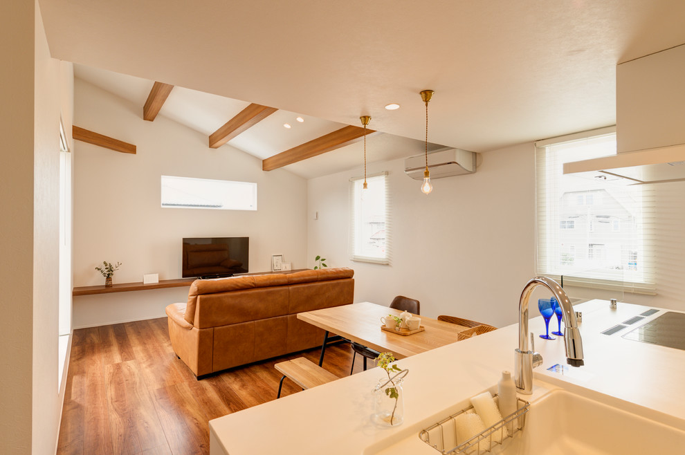 Kleines, Offenes Asiatisches Wohnzimmer mit weißer Wandfarbe, braunem Holzboden, freistehendem TV und braunem Boden in Sonstige