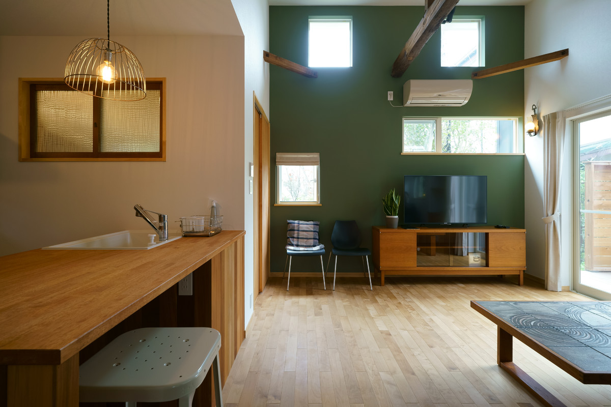 Modernes Wohnzimmer mit grüner Wandfarbe, braunem Holzboden, freistehendem TV und braunem Boden in Tokio