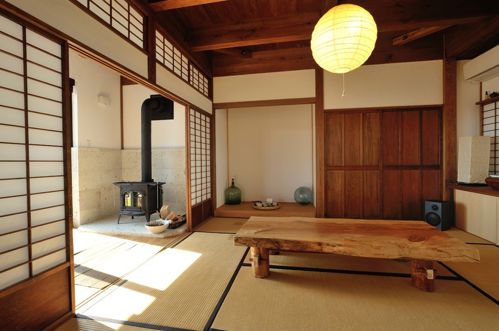 Asiatisk inredning av ett vardagsrum, med vita väggar, tatamigolv, en öppen vedspis, en spiselkrans i betong och brunt golv