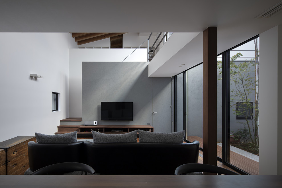 Imagen de salón abierto moderno con paredes blancas, suelo de madera en tonos medios, televisor colgado en la pared y suelo marrón