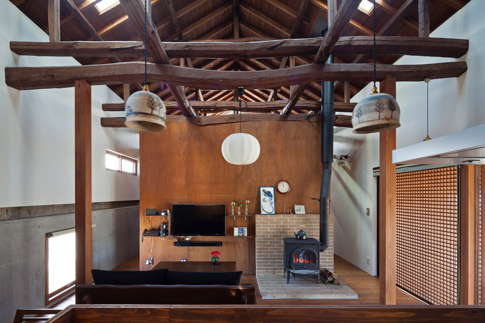 Esempio di un soggiorno etnico aperto con pareti bianche, TV a parete, pavimento in legno massello medio, stufa a legna e cornice del camino in mattoni