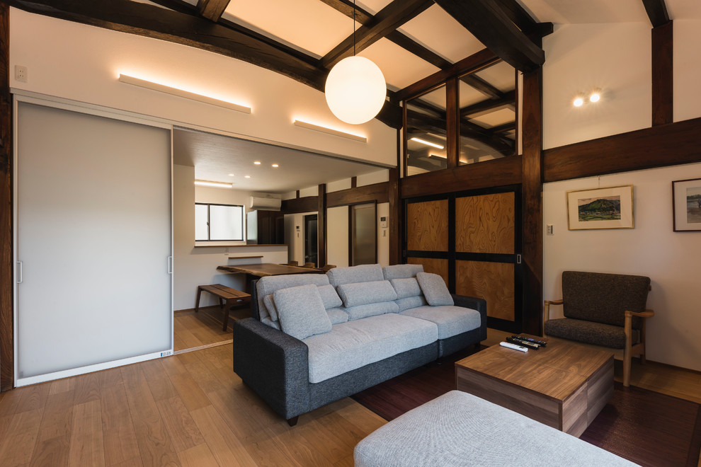 Offenes Asiatisches Wohnzimmer ohne Kamin mit weißer Wandfarbe, Sperrholzboden, freistehendem TV und braunem Boden in Sonstige