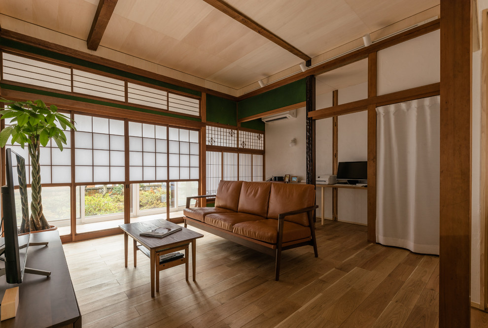 Mittelgroßes, Offenes Asiatisches Wohnzimmer ohne Kamin mit weißer Wandfarbe, braunem Holzboden und freistehendem TV in Sonstige