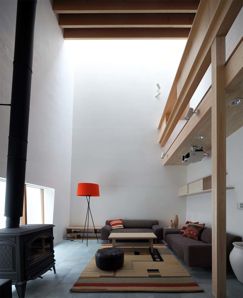 This is an example of a contemporary living room in Kyoto with white walls, a wood burning stove, a stone fireplace surround and grey floors.