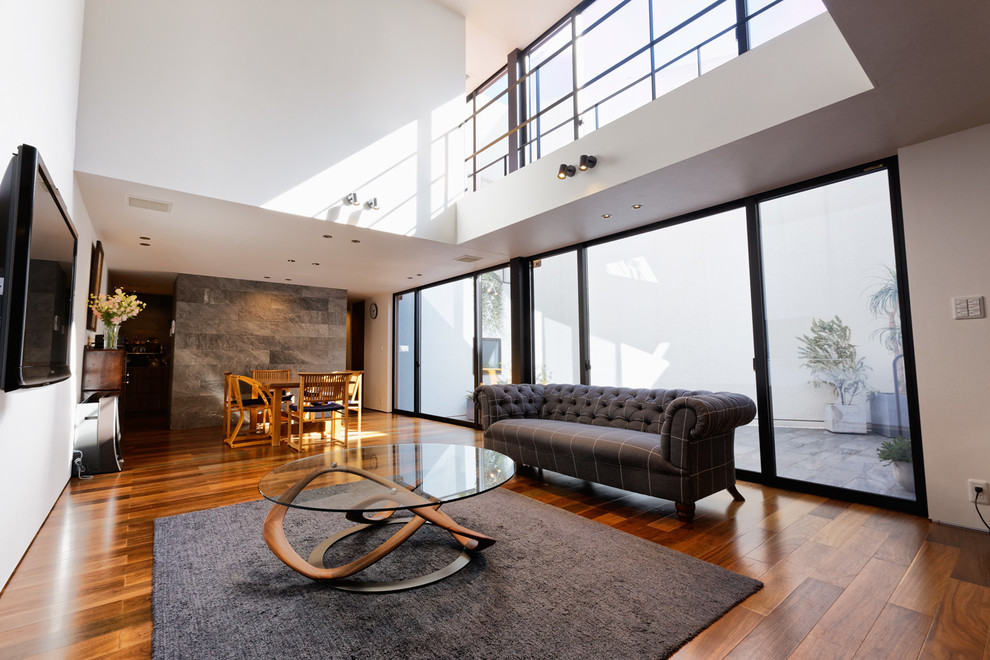 Immagine di un soggiorno contemporaneo con pareti bianche, pavimento in legno massello medio, nessun camino, TV a parete e pavimento marrone