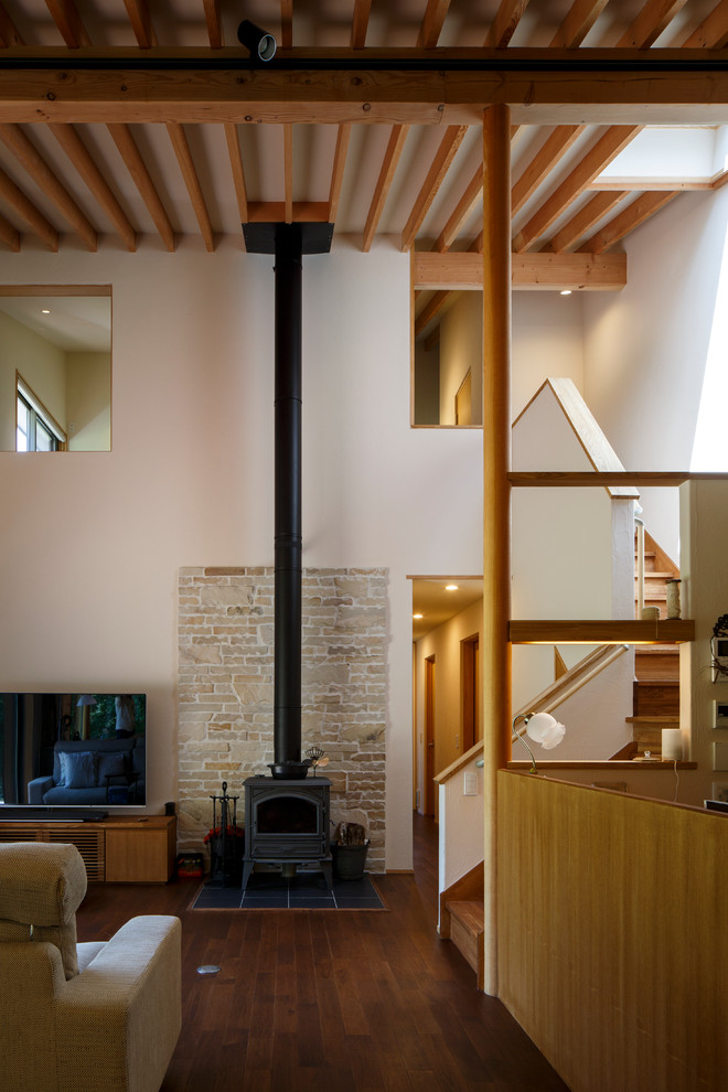 This is an example of a modern open plan living room in Other with dark hardwood flooring, a wood burning stove, a stone fireplace surround, a freestanding tv and brown floors.