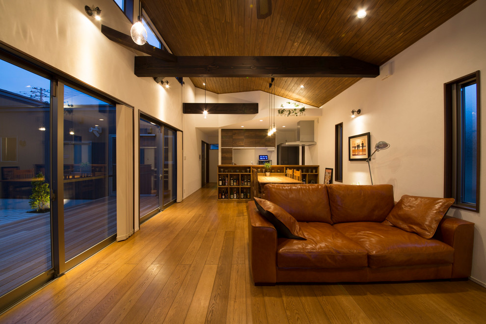 Offenes Asiatisches Wohnzimmer mit weißer Wandfarbe, braunem Holzboden, freistehendem TV und braunem Boden in Sonstige
