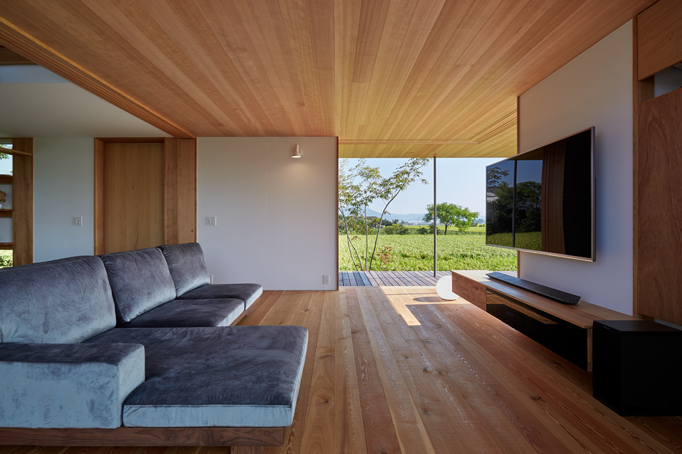 Modelo de salón abierto de estilo zen con paredes blancas, suelo de madera en tonos medios, televisor colgado en la pared y suelo marrón