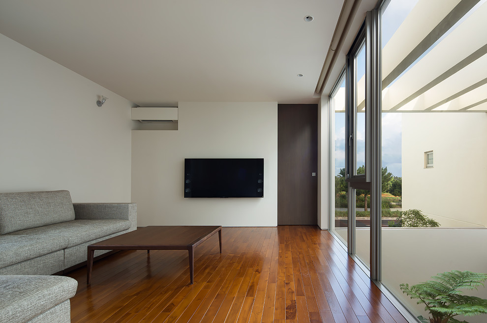 Imagen de salón minimalista con paredes blancas, suelo de madera oscura, televisor colgado en la pared y suelo marrón
