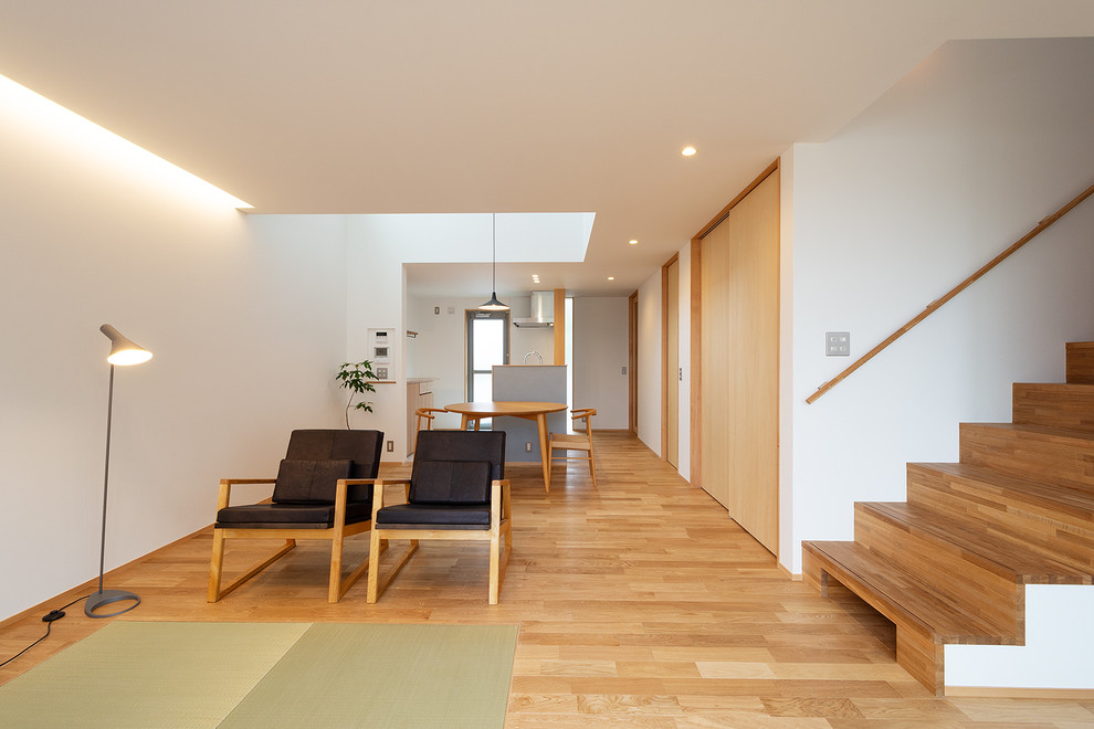 Cette image montre un salon asiatique ouvert avec un mur blanc, un sol en bois brun et un sol marron.