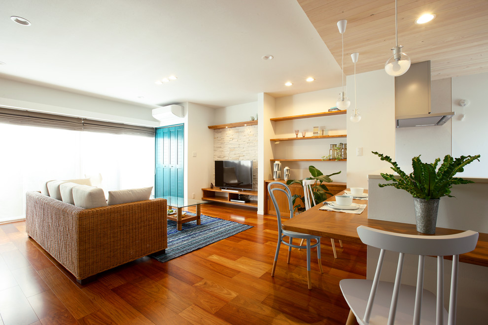 Immagine di un soggiorno tropicale con pareti bianche, pavimento in legno massello medio, TV autoportante e pavimento marrone